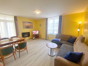 A living room with a sofa, a small round table, a TV, and a dining area with chairs and a table.