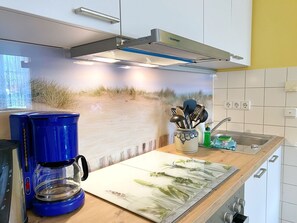 A kitchen with a coffee maker, utensils, and a sink.