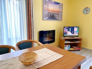Ein Essbereich mit Holztisch, Stühlen, einem gewebten Korb, Kamin, Fernseher und Bücherregal.