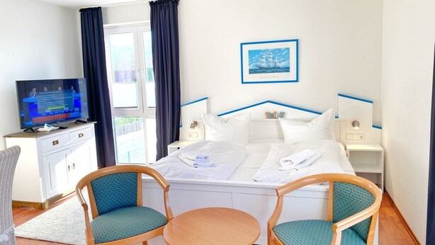 Ett hotellrum med en säng, två stolar, ett litet bord, en tv och ett fönster med gardiner.