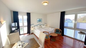 Ett hotellrum med en säng, en tv, ett matbord och ett fönster med gardiner.