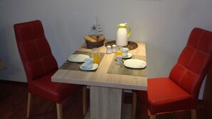 Een eettafel met twee rode stoelen, een ontbijtsetting met brood, eieren en een karaf, en een schilderij van een zonsondergang boven een brug aan de muur.