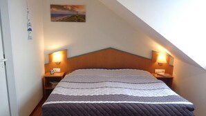 Een slaapkamer met een schuine plafond, een bed met een gewatteerde sprei, twee bedlampjes en een foto aan de muur.