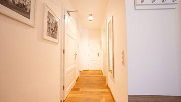 A hallway with wooden flooring, white walls, and framed pictures on the left.