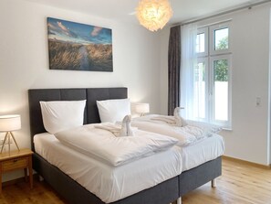 Quarto moderno com uma cama grande, mesa de cabeceira, luminária e janela com cortinas.