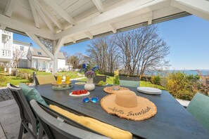 An outdoor dining area with a view of the sea, a table set with plates, glasses, and a decorative hat.