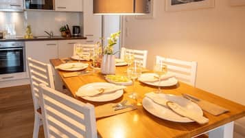A modern kitchen with white cabinetry, a wooden dining table set for four, and a large window above the table.