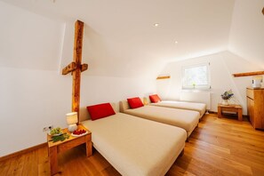 A room with two beds, a wooden cross, a small table with a lamp, and a window with a view.
