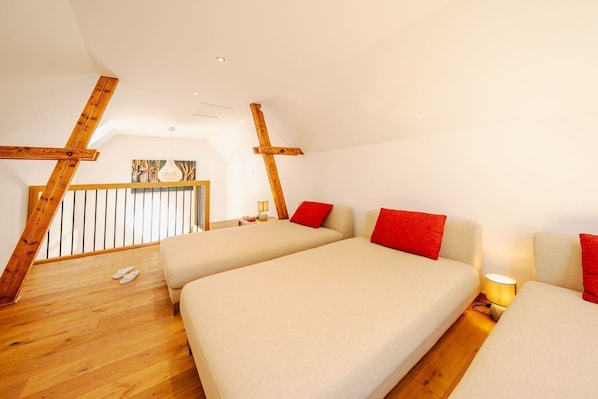 Ein Zimmer mit hohen Decken, Holzbalken, zwei Betten mit roten Kissen, Holzboden und einem Balkon mit Geländer.