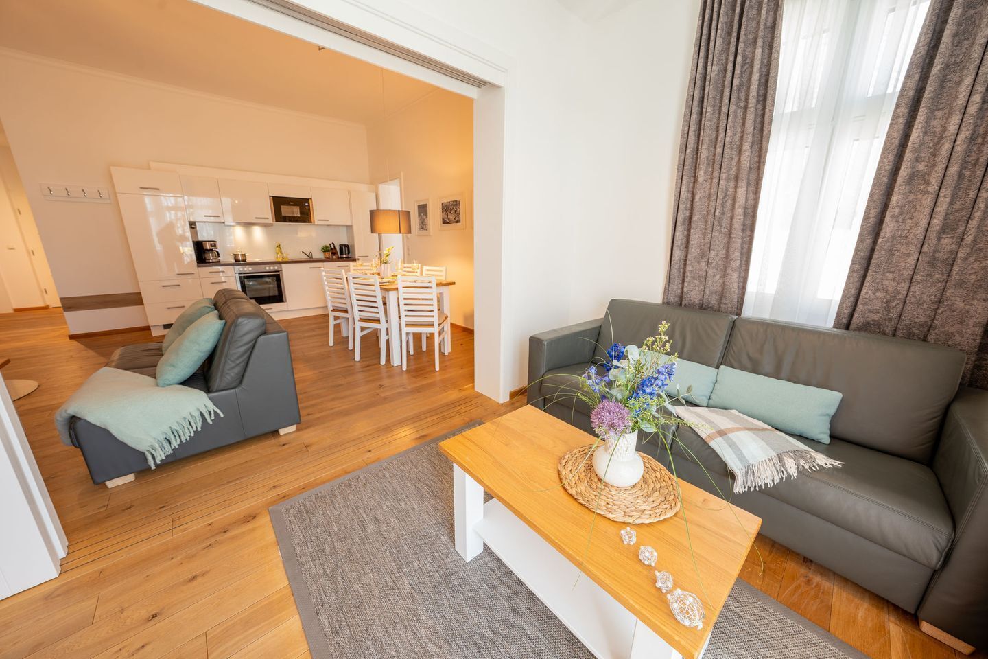 Een moderne woonkamer met een bank, een houten salontafel en een eethoek op de achtergrond.