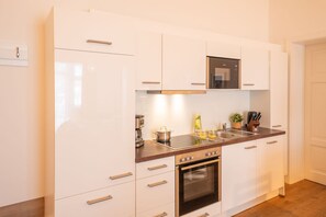 Une cuisine moderne avec des meubles blancs, un four encastré, une plaque de cuisson et un four à micro-ondes.