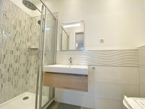 Een moderne badkamer met een glazen douchecabine, een wit wastafelmeubel met een houten kast, en een grote spiegel boven de wastafel.