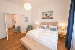 A hotel room with a bed, two bedside tables, a bench, a door, and a chair.