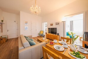 A modern living room with a sofa, dining table, chandelier, and a television. - Villa Jenny - Apartment 1 - Villa Jenny Sassnitz (Sassnitz)