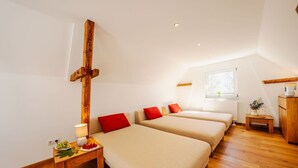 Une chambre avec deux lits, un crucifix en bois, une petite table avec une lampe et une fenêtre donnant sur un beau paysage.