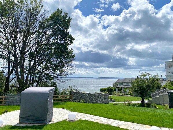 Een aangelegde tuin met een kiezelpad, een overdekte barbecue en uitzicht op zee.