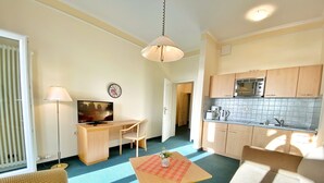 A compact living space with a kitchenette, a dining area, and a seating area with a television and lamp. - Sea view apartment no. 21 in the Villa Anna in Sassnitz on Rügen - Sassnitz - (Sassnitz)