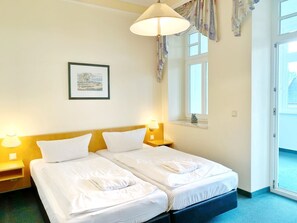 Quarto de hotel com duas camas, um quadro pendurado na parede e uma janela com cortinas.