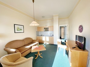 A compact living space with a sofa, a small table, a TV, and a kitchenette.