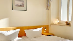 A hotel room with a bed, pillows, a bedside table with a lamp, a window with a view, and a framed picture on the wall. - Sea view apartment no. 32 in the Villa Anna in Sassnitz on Rügen - Sassnitz - (Sassnitz)