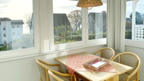 Una habitación con una mesa y sillas, ventanas amplias que dan a edificios y árboles, y una lámpara colgante.