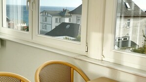 Habitación con un ventanal grande con vistas a la costa, que incluye una mesa y dos sillas de mimbre.