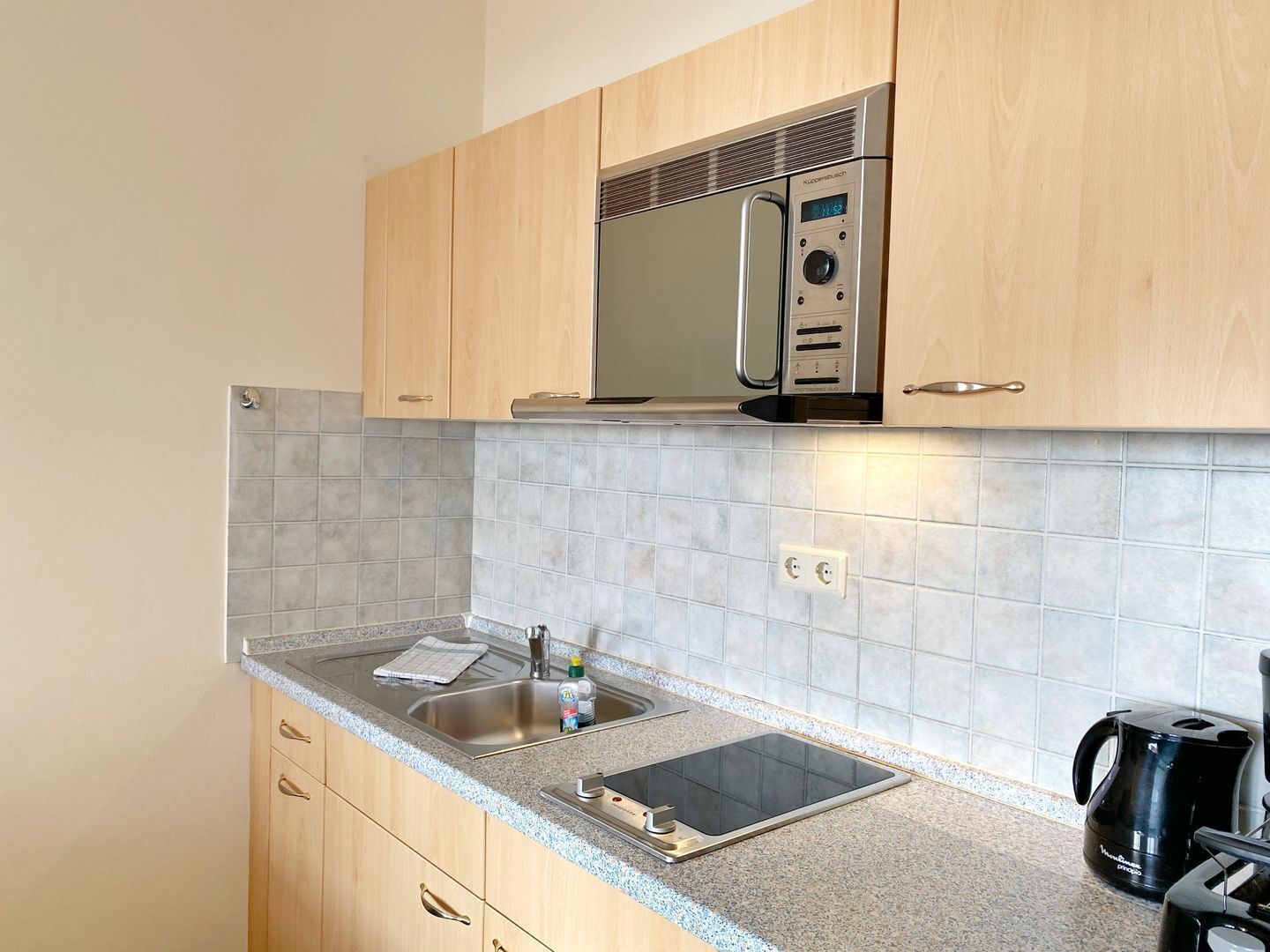 Een keuken met een magnetron, spoelbak en waterkoker.