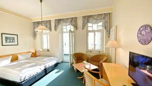A hotel room with a bed, a desk with a chair, a television, and a window with curtains. - Sea view apartment no. 22 in the Villa Anna in Sassnitz on Rügen - Sassnitz - (Sassnitz)