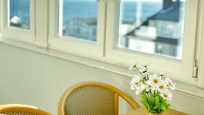 A room with a window overlooking a coastal view, a table with a vase of flowers, and a chair. - Sea view apartment no. 22 in the Villa Anna in Sassnitz on Rügen - Sassnitz - (Sassnitz)