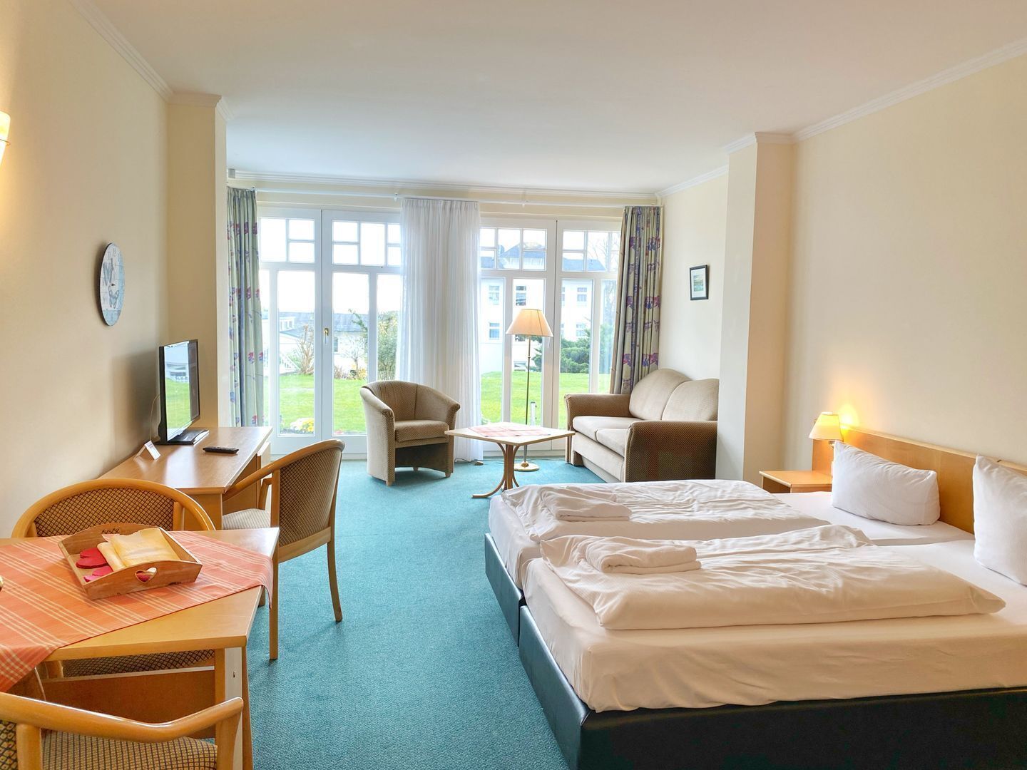 Ein Hotelzimmer mit einem Bett, zwei Sesseln, einem Schreibtisch mit Computer und Blick ins Freie.