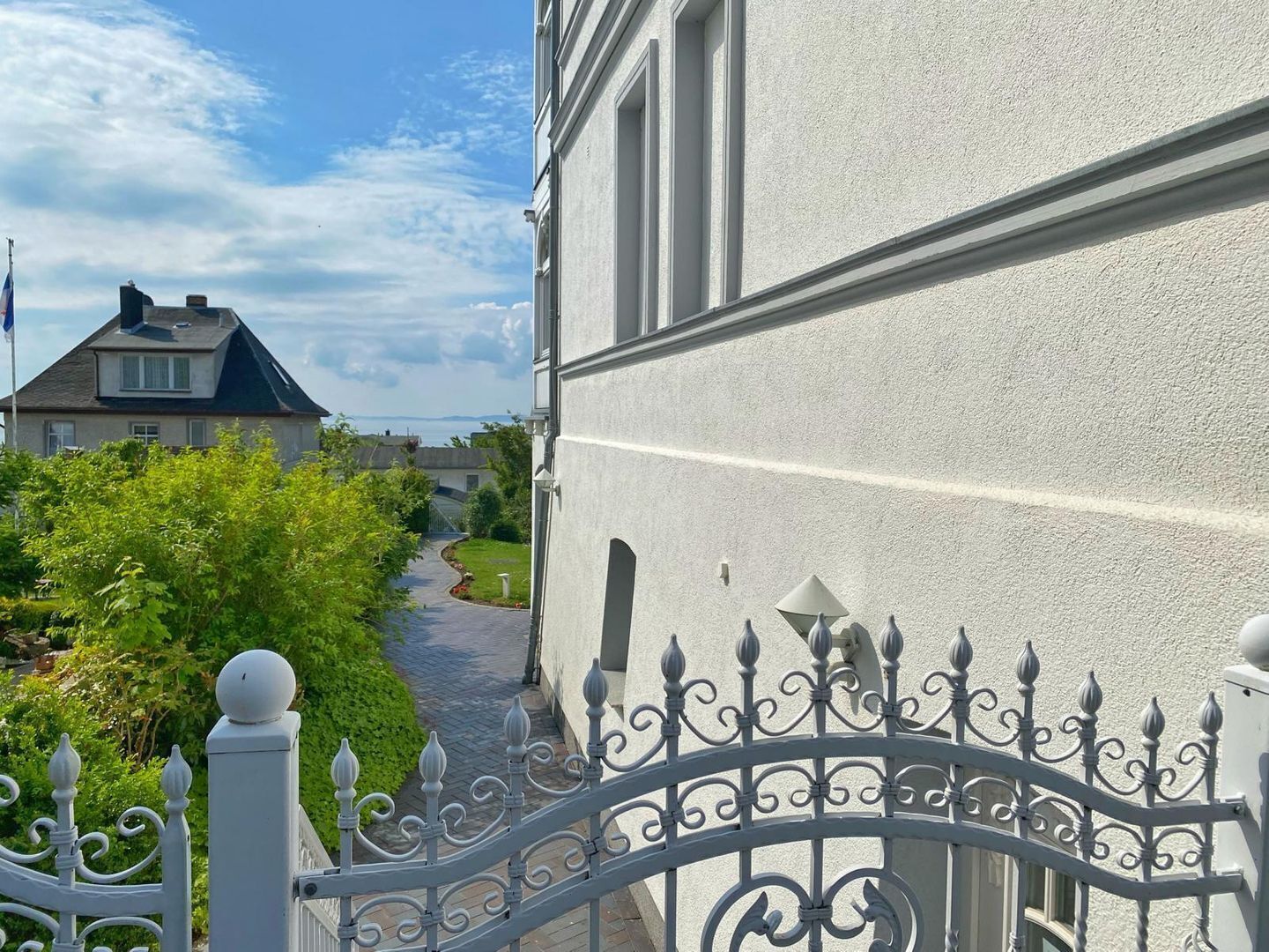 Ein verschlossenes Tor mit schmiedeeisernem Gitter, ein Weg zu einem Haus und ein klarer Himmel.
