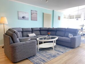 Ein modernes Wohnzimmer mit einem grauen Ecksofa, einem kleinen runden Couchtisch und einem blauen Teppich mit Muster.