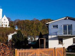 A residential area with a white building with a tower, a modern house, and a wooden fence.