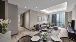 A modern living room with a grey sofa, a coffee table, and a dining area with a table set for two. - 25hours Hotel Jakarta The Oddbird (Jakarta)