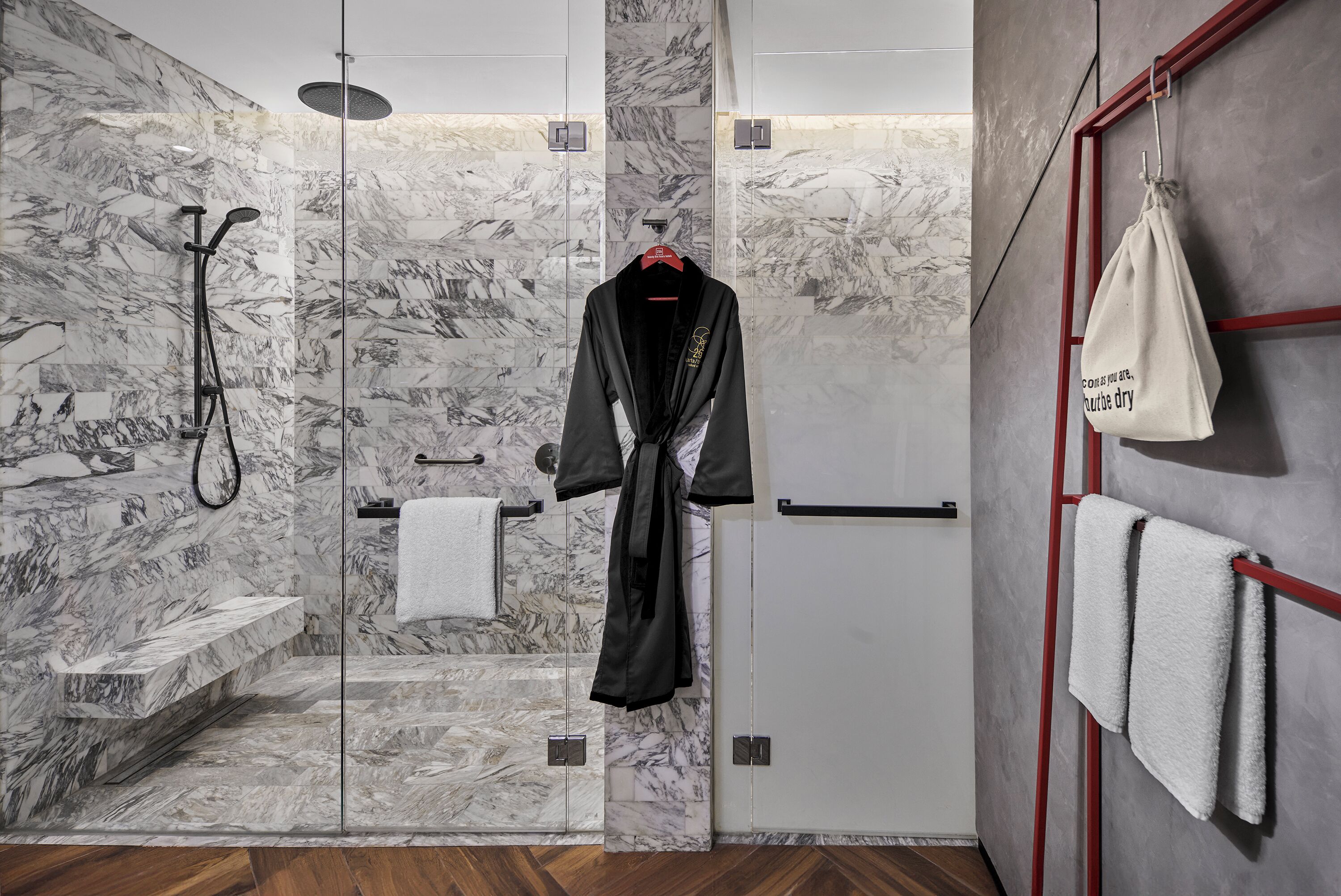 Un baño moderno con ducha de vidrio, paredes de mármol y suelo de madera.