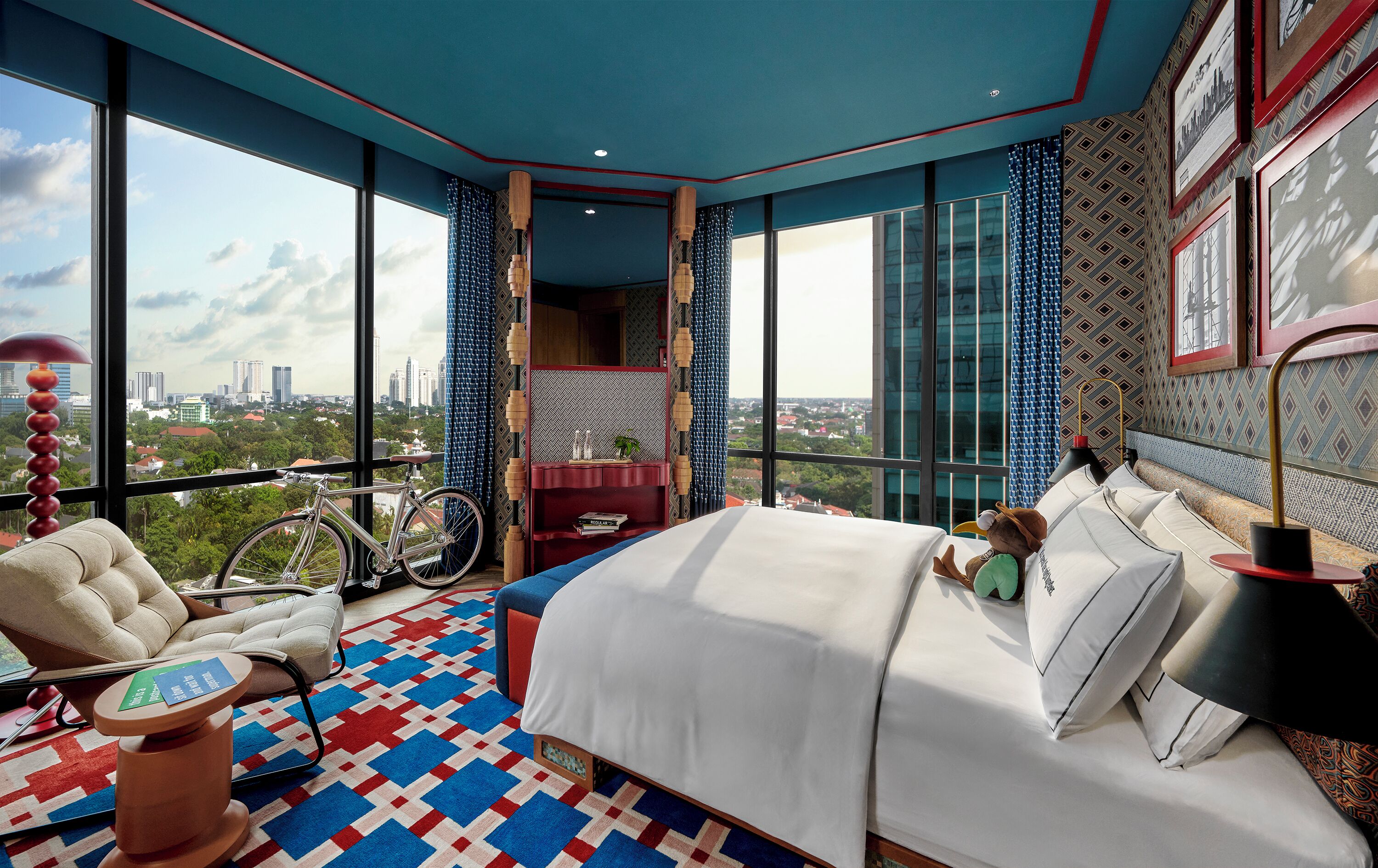 Un dormitorio moderno con una cama grande, una silla, una bicicleta y vistas a la ciudad.