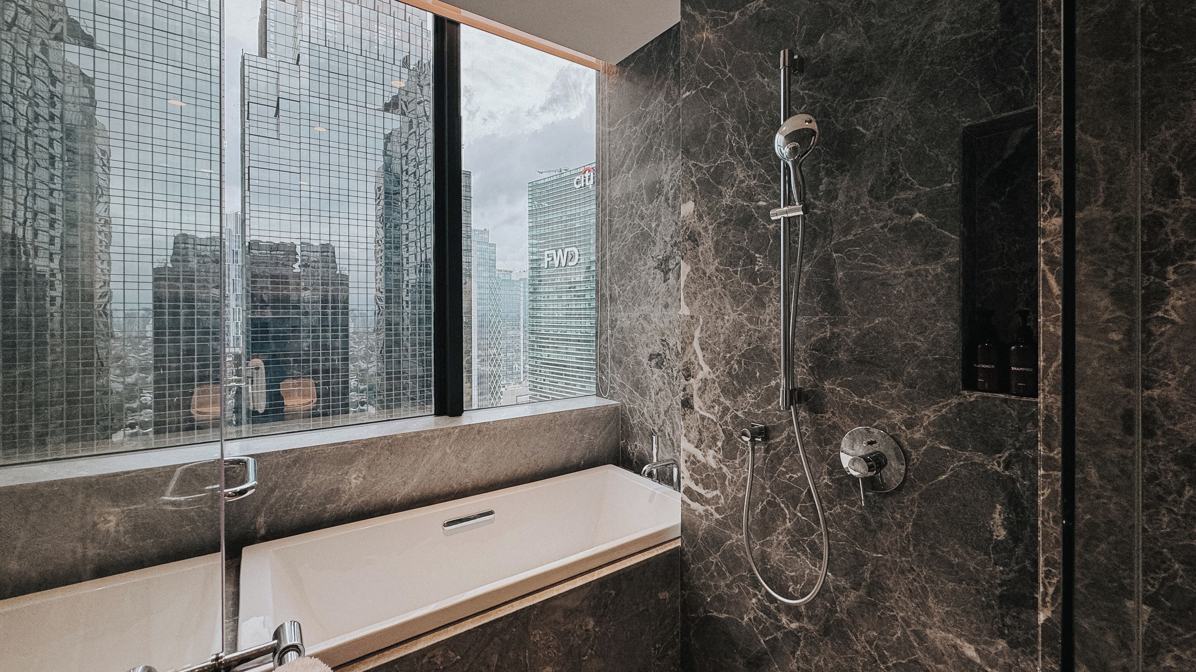 Un baño moderno con un ventanal amplio, pared de mármol y ducha integrada.