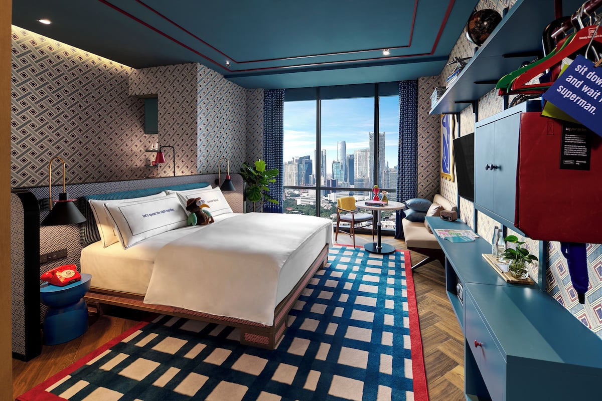A modern hotel room with a large bed, a desk, and a view of the city skyline.
