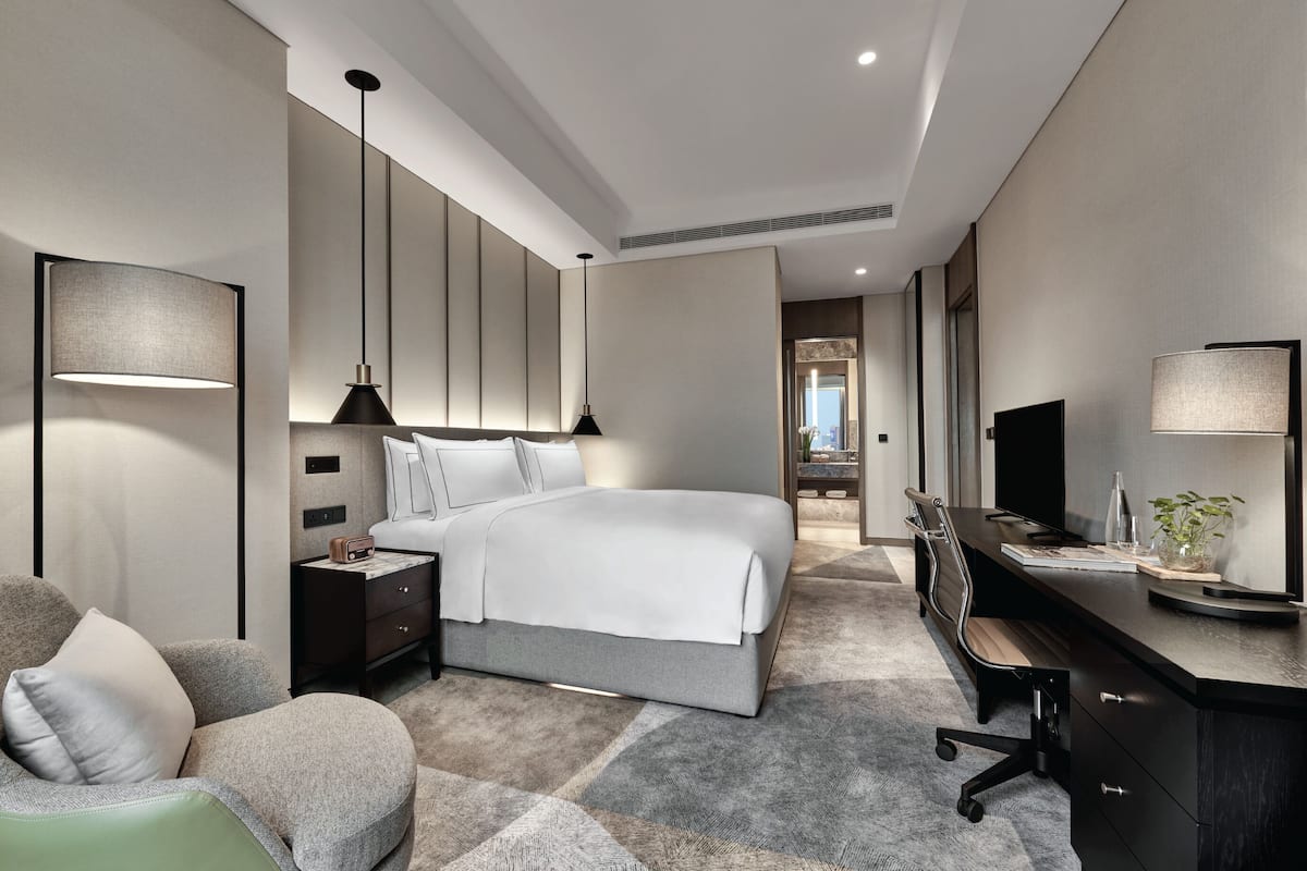 A modern hotel room with a large bed, a desk, a chair, and a TV.
