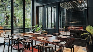 Comedor con una larga mesa dispuesta para cuatro personas, sillas alrededor y vistas a zonas verdes a través de amplios ventanales.