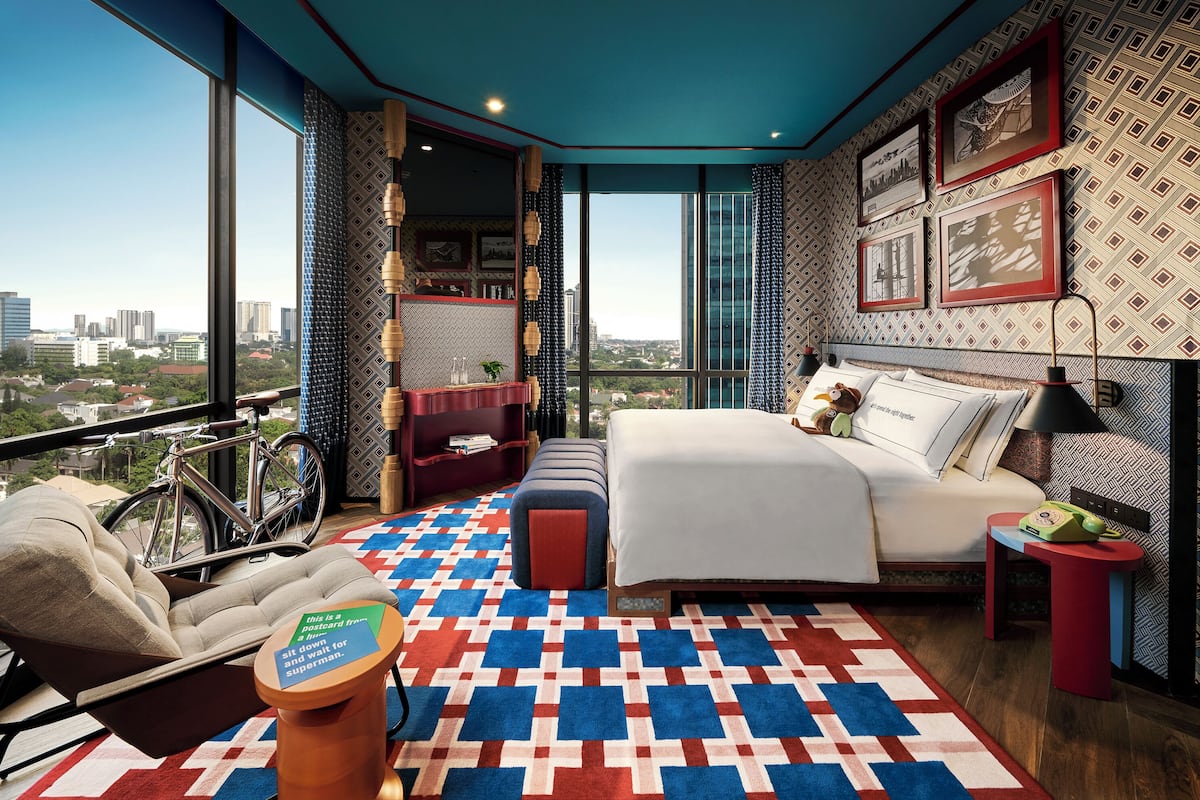 A modern bedroom with a large window, a bed, a chair, a small table, and a bicycle.