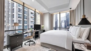 A modern hotel room with a large bed, a desk with a computer, a chair, and a TV. The room has large windows offering a city view. - 25hours Hotel Jakarta The Oddbird (Jakarta)