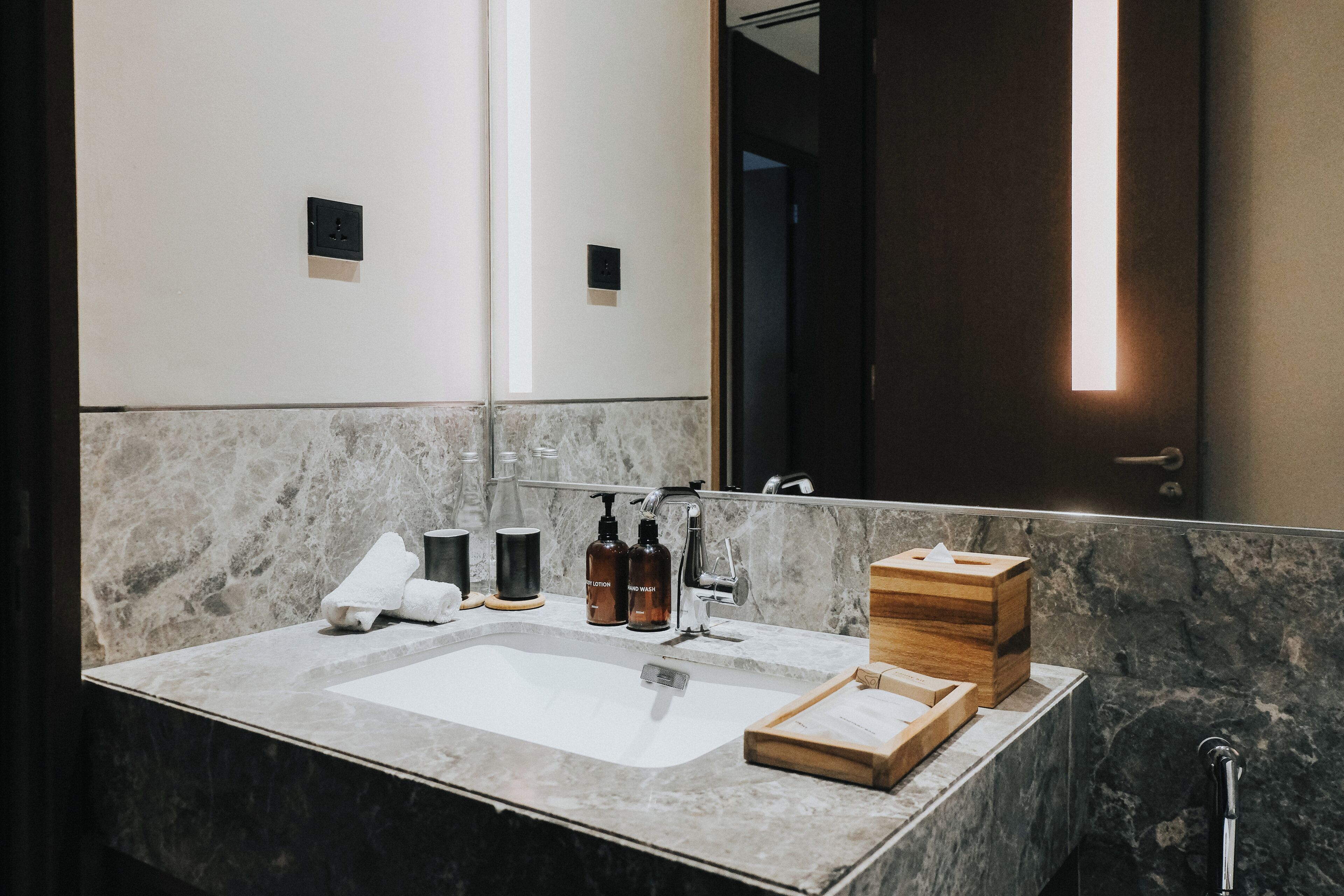 A modern bathroom with a marble sink, a mirror, and a wooden box on the counter.