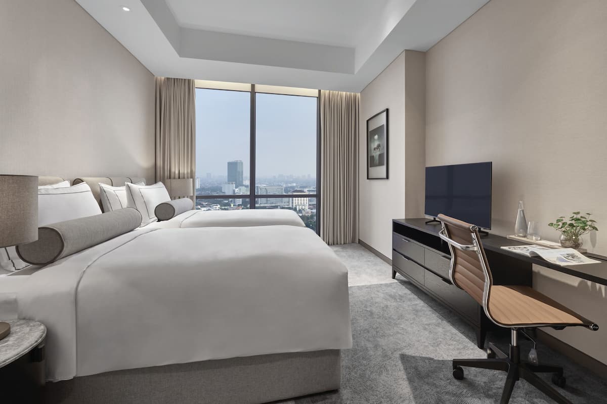 A modern hotel room with a large bed, a desk, a chair, a TV, and a view of the city.