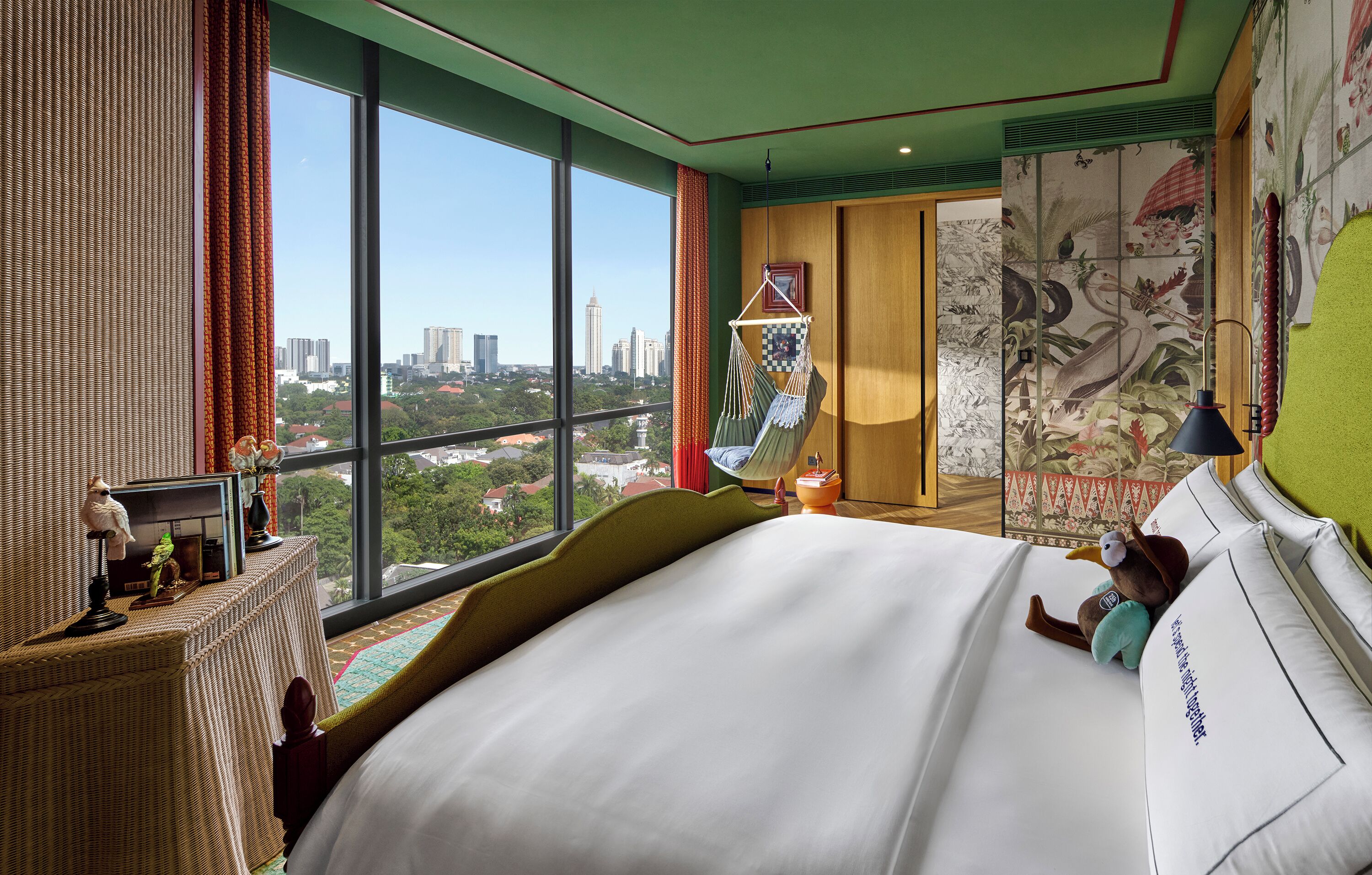 Quarto de hotel com uma cama grande, vista da cidade, uma rede e um painel decorativo.