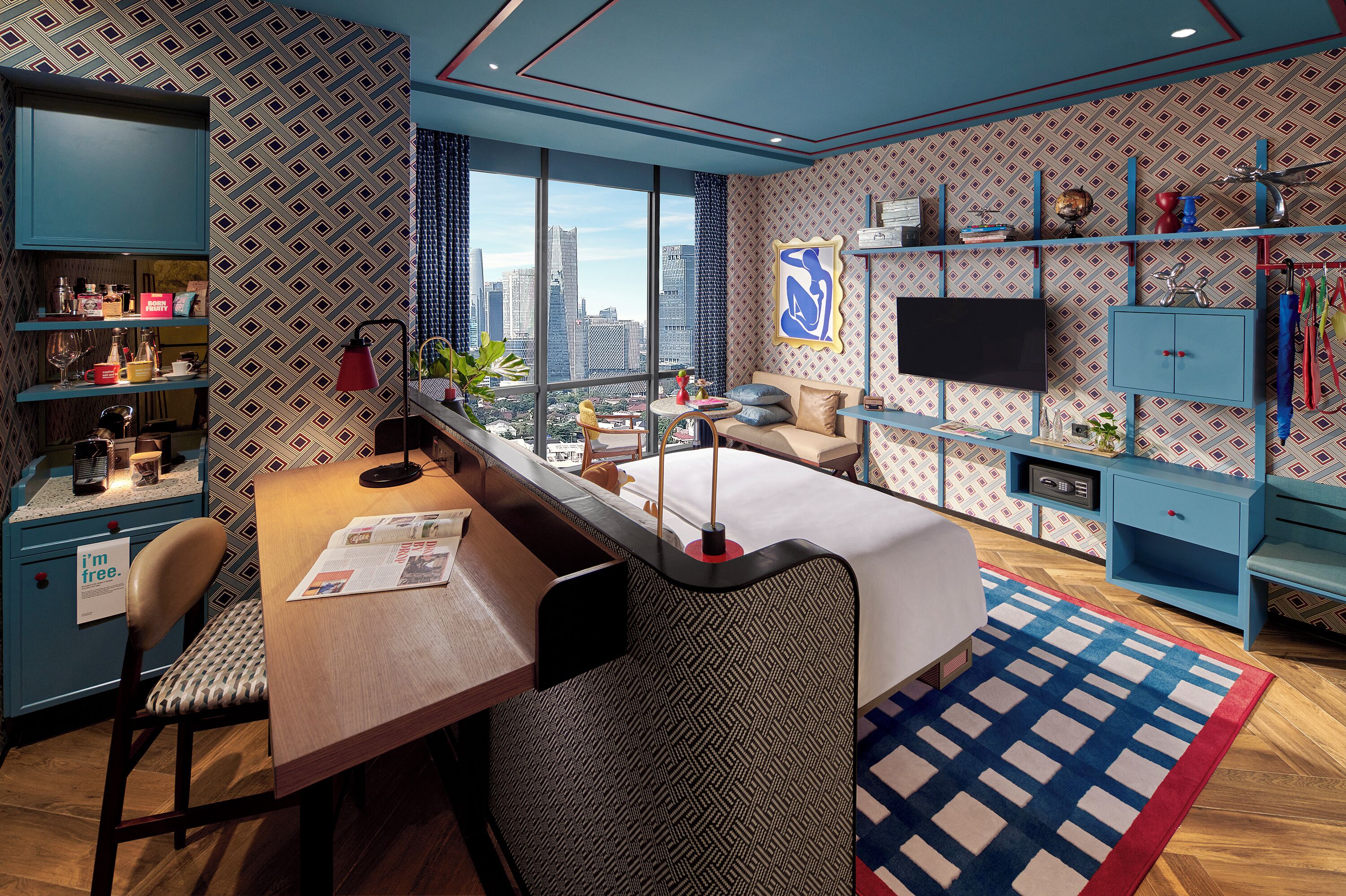 A modern hotel room with a large window, a sofa, a dining table, and a TV.