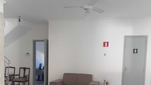 A living room with a beige sofa, a patterned rug, a ceiling fan, and a fire extinguisher. - Pousada Baraúna (Santos)