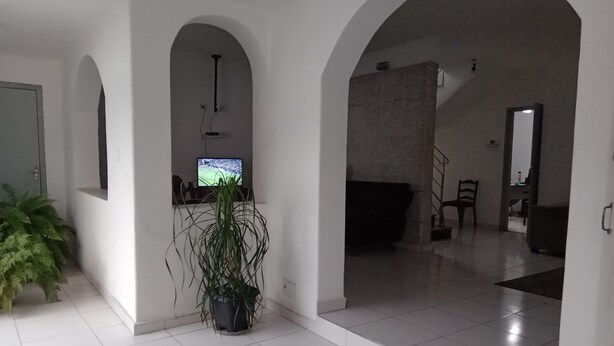 A spacious living area with a tiled floor, a potted plant, a television, and a staircase leading to another level. - Pousada Baraúna (Santos)
