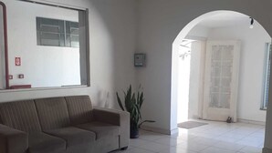 A living room with a sofa, a potted plant, a patterned rug, and a tiled floor. - Pousada Baraúna (Santos)
