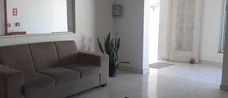 A living room with a sofa, a potted plant, a patterned rug, and a tiled floor.